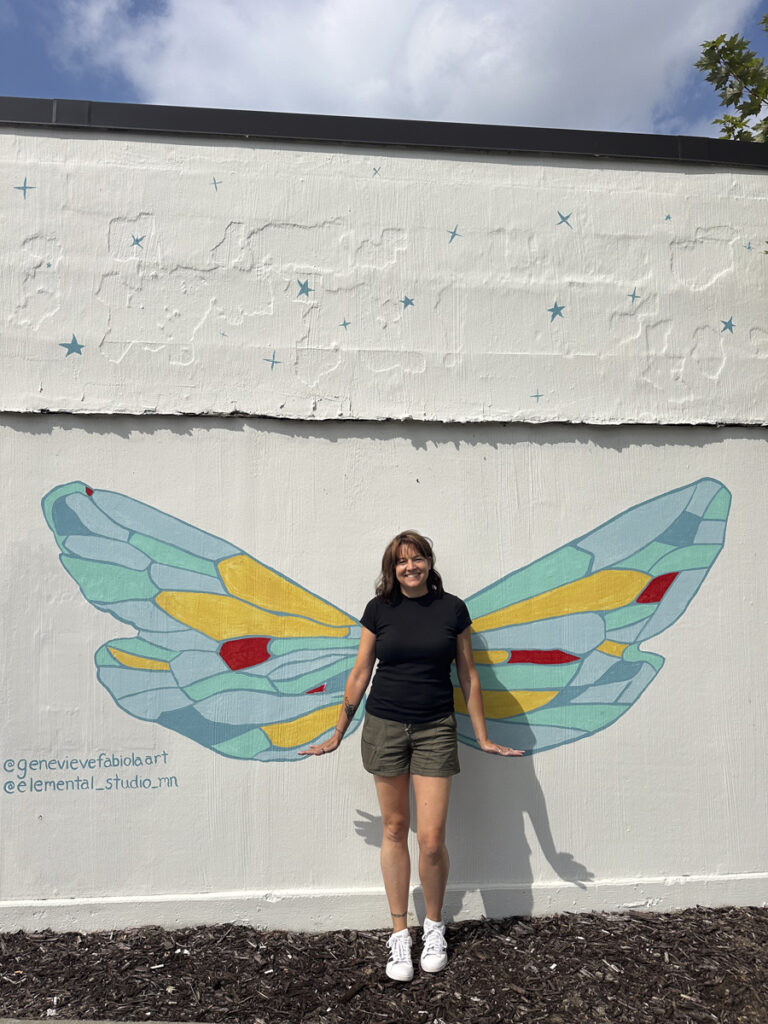 Woman standing in front of butterfly wing mural. 