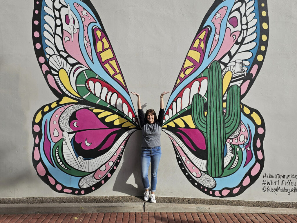 Woman standing in front of butterfly wings mural. 